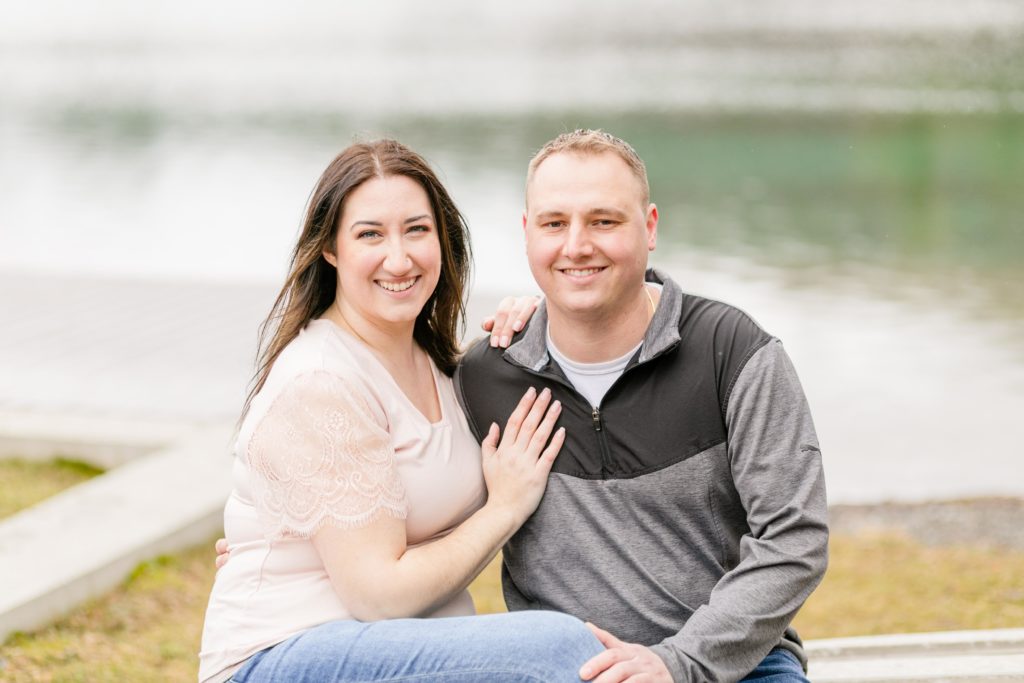Engaged couple sitting next to each other with hand on chest at their Engagement Session