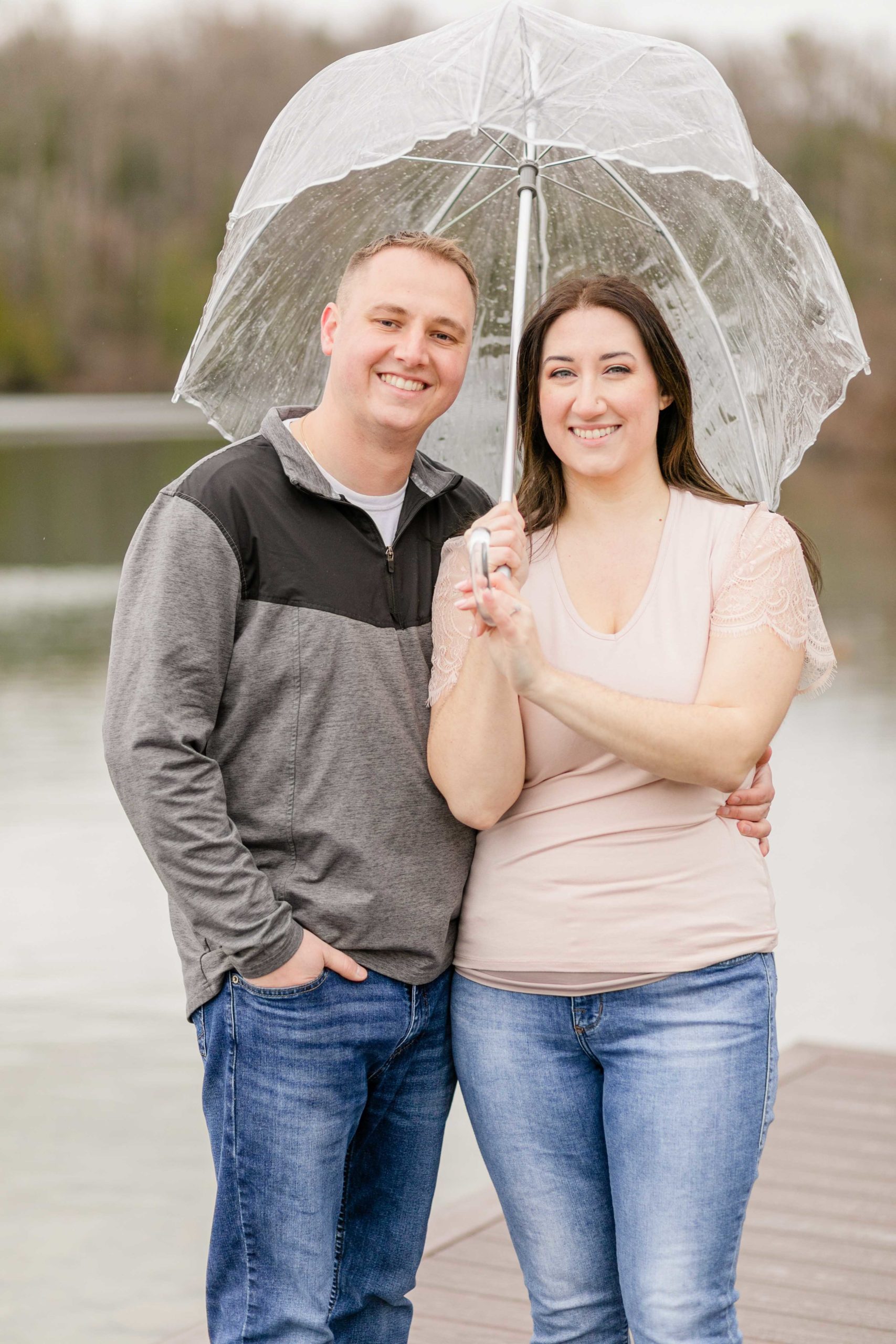 Engaged couple standing next to each other at Green Lakes with an umbrella in the rain. 