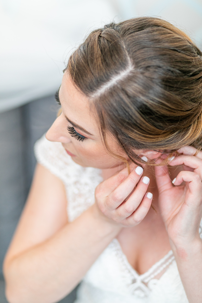 bride putting on her earrings while getting ready